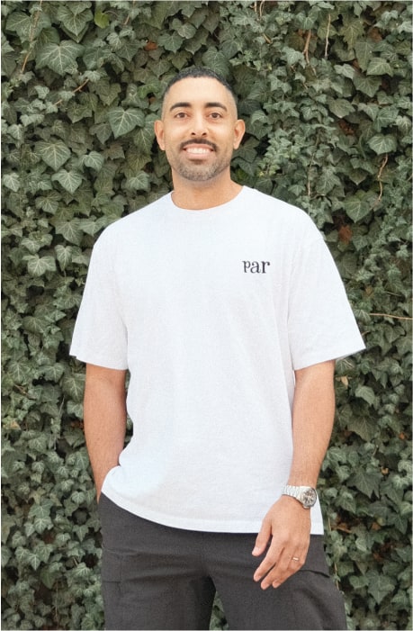 Headshot photograph. White shirt, in front of a green vine wall.